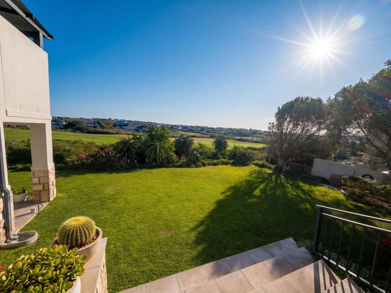 A well-maintained rear garden featuring a tiled patio, stone-clad pillar, and expansive views over the surrounding landscape.