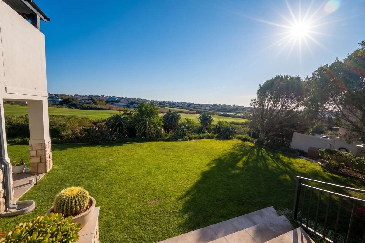 A well-maintained rear garden featuring a tiled patio, stone-clad pillar, and expansive views over the surrounding landscape.