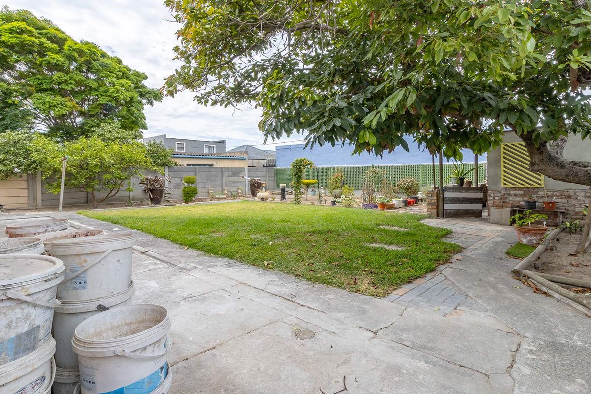 A spacious rear garden featuring a central lawn, mature tree, and concrete patio area enclosed by boundary walls.