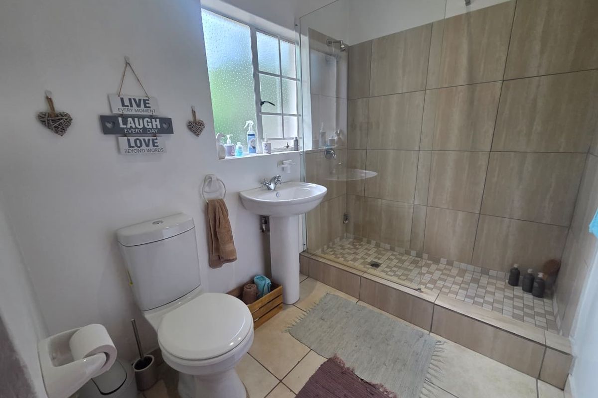 A functional bathroom featuring a walk-in shower with glass enclosure, pedestal basin, and toilet, finished with neutral floor and wall tiling.