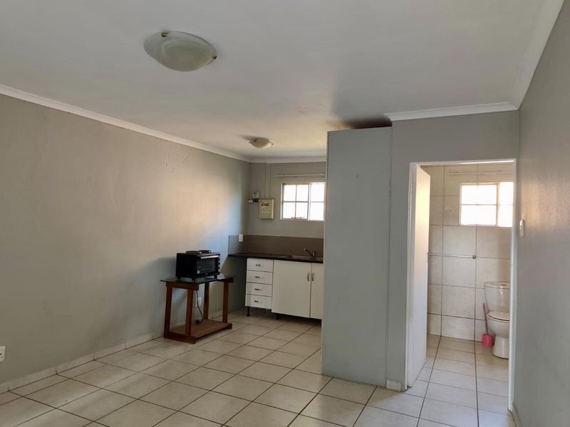 Open plan living area featuring a compact kitchenette with built-in cabinetry and an adjacent tiled bathroom with a toilet.