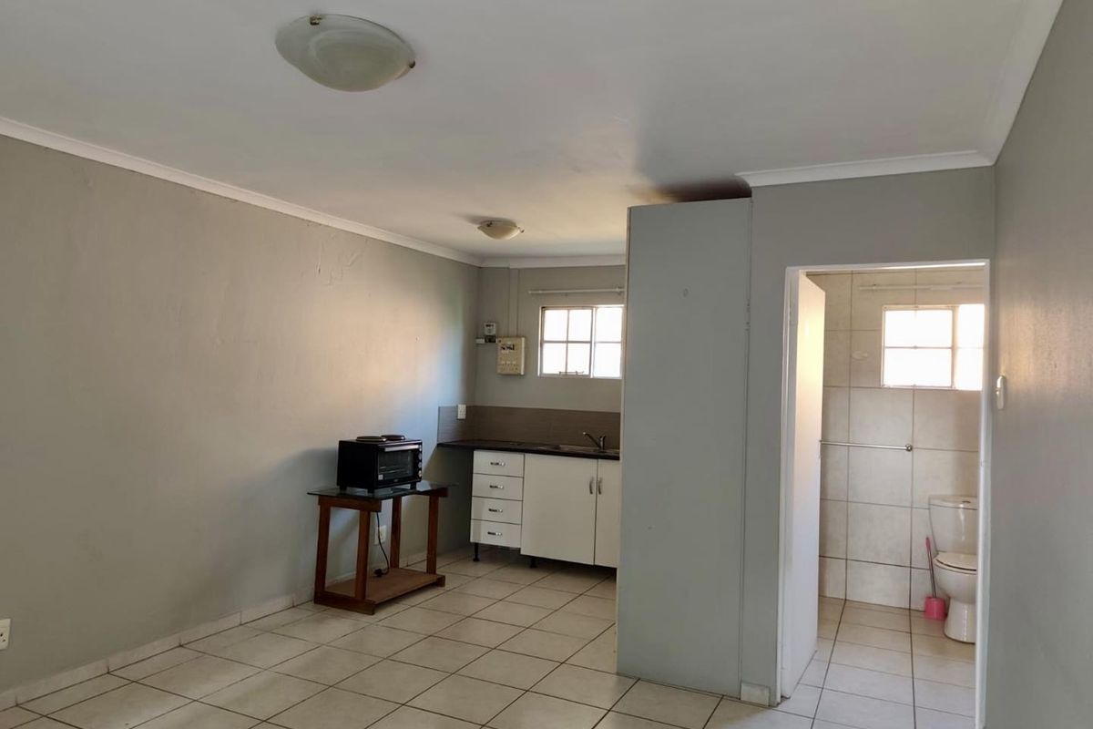 Open plan living area featuring a compact kitchenette with built-in cabinetry and an adjacent tiled bathroom with a toilet.