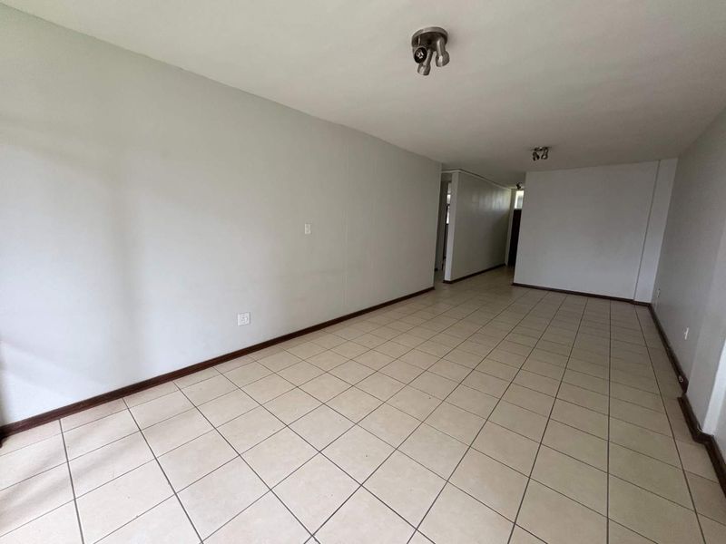 A spacious, empty living area featuring neutral tiled flooring and simple ceiling-mounted lighting, offering a blank canvas for interior design.
