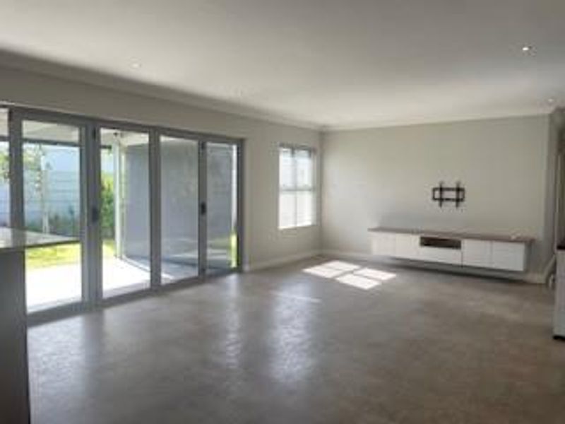 Spacious, light-filled living area featuring polished concrete floors, recessed lighting, and large sliding stacker doors opening to the outdoor patio.