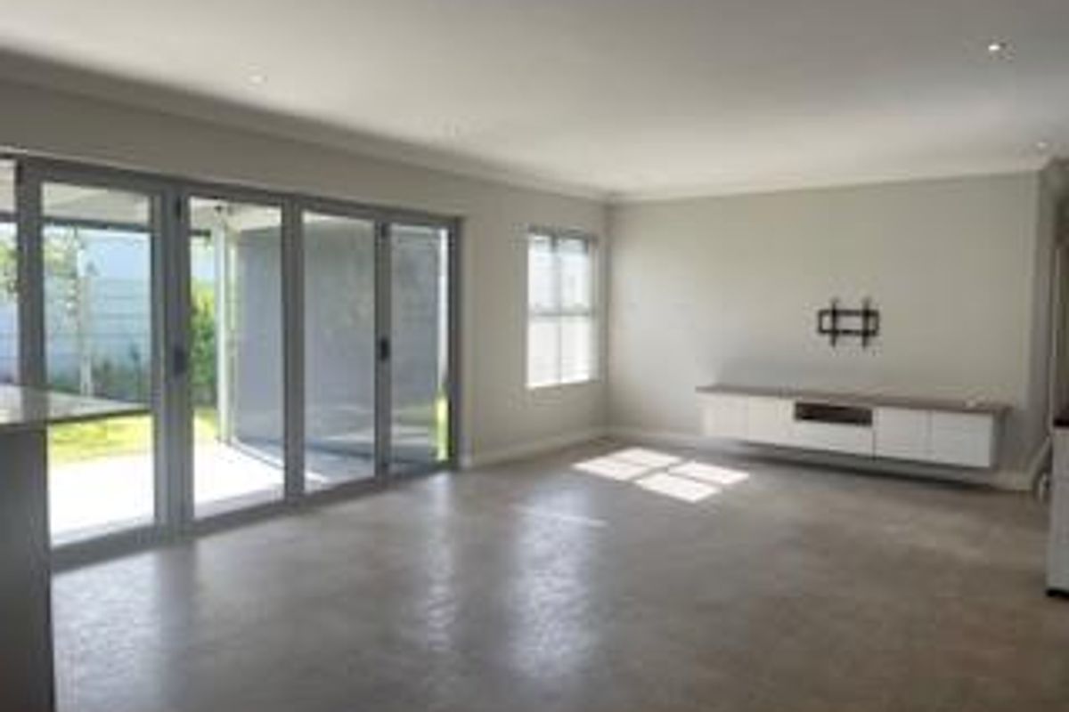 Spacious, light-filled living area featuring polished concrete floors, recessed lighting, and large sliding stacker doors opening to the outdoor patio.