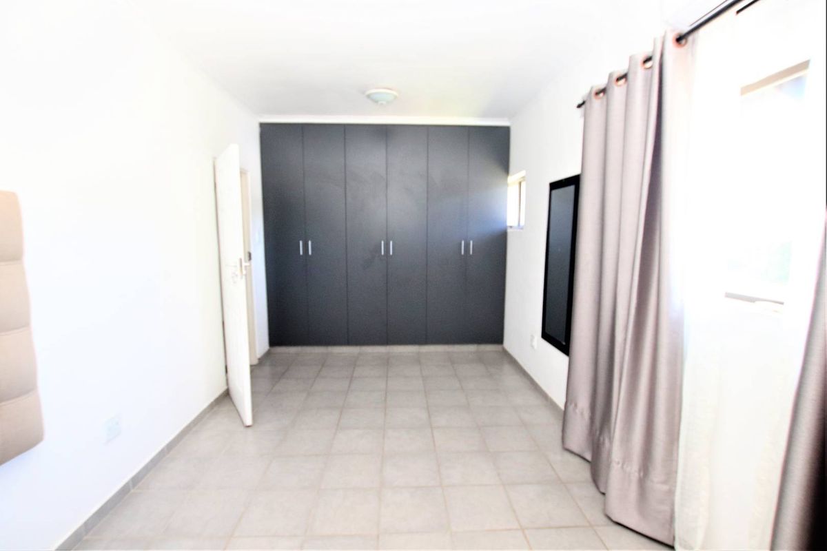 A clean, empty bedroom featuring neutral tiled flooring and dark grey built-in cupboards, offering a versatile space ready for personalization.