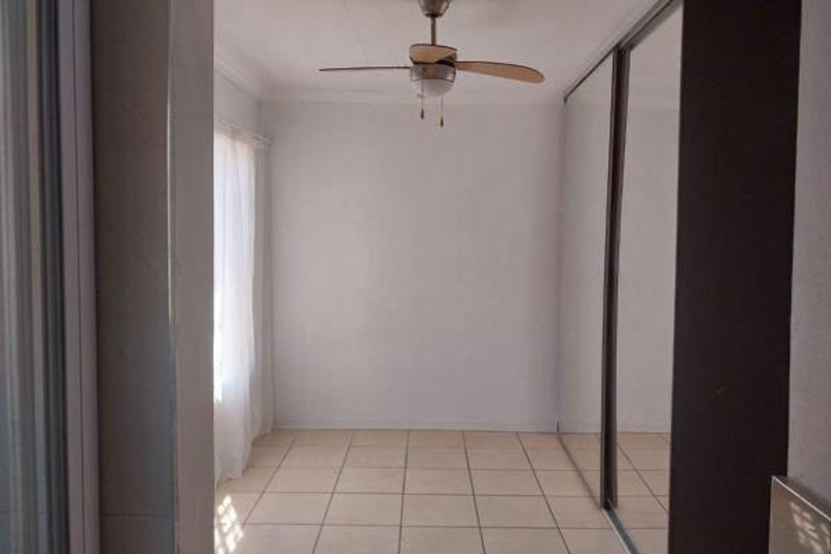 An empty bedroom featuring tiled flooring, a ceiling fan, and a large built-in wardrobe with sliding mirror doors.