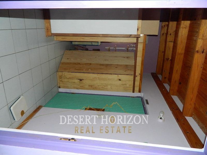A small utility or storage space featuring tiled walls, exposed timber rafters, and a wooden storage enclosure with an access hatch.