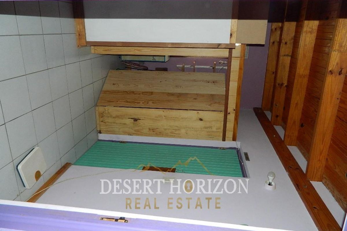 A small utility or storage space featuring tiled walls, exposed timber rafters, and a wooden storage enclosure with an access hatch.