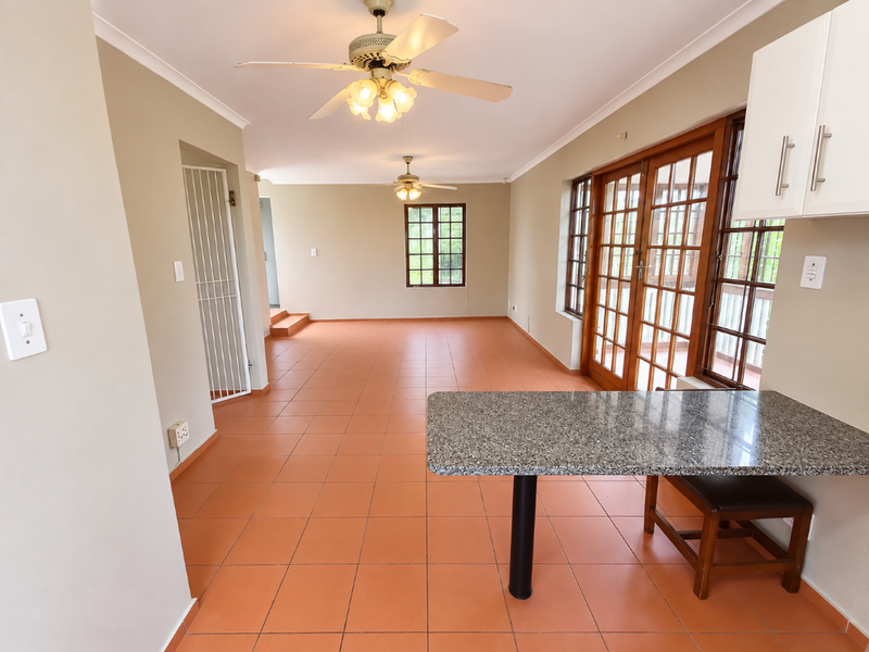 Spacious open-plan living area featuring tiled flooring, dual ceiling fans, a granite breakfast bar, and timber-framed glass doors leading to the exterior.