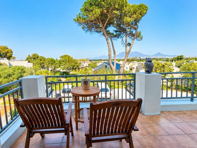 A spacious balcony featuring tiled flooring and metal balustrades, offering scenic views of the surrounding estate and distant mountains.