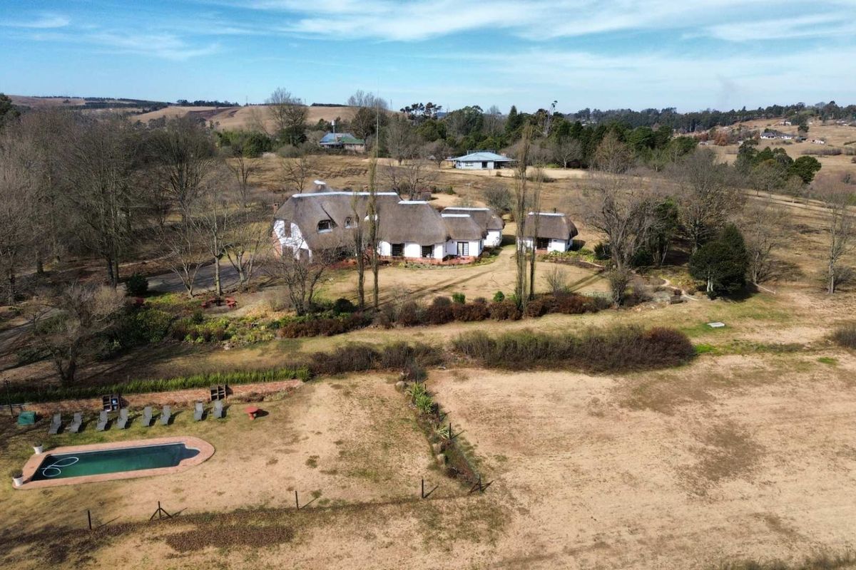 Aerial view of a rural property featuring a traditional thatched-roof house, a swimming pool, and expansive surrounding grounds.