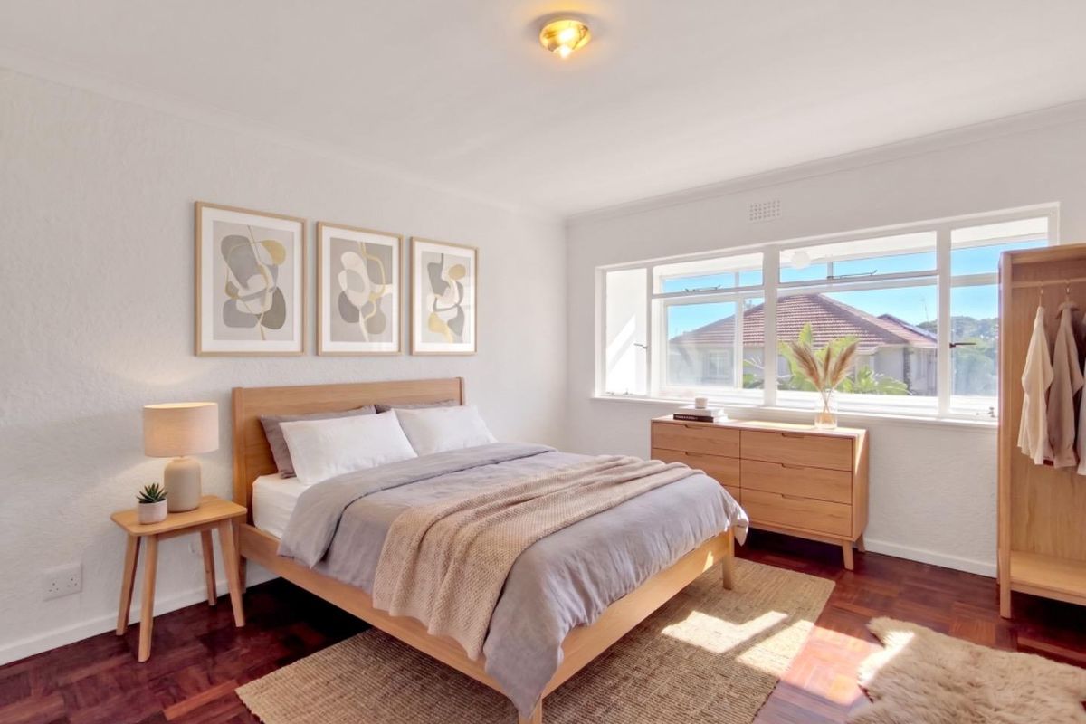 A bright and well-maintained bedroom featuring warm parquet flooring, a large window providing natural light, and neutral wall finishes.