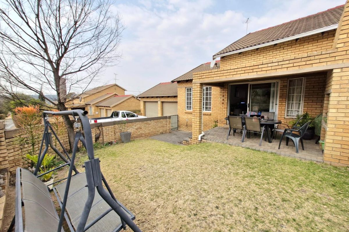 A rear view of the cluster home featuring a covered patio, paved area, and a private garden space.