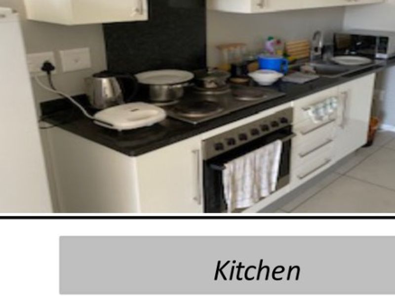 A compact kitchen featuring white cabinetry, dark stone countertops, an integrated electric hob, oven, and extractor fan.