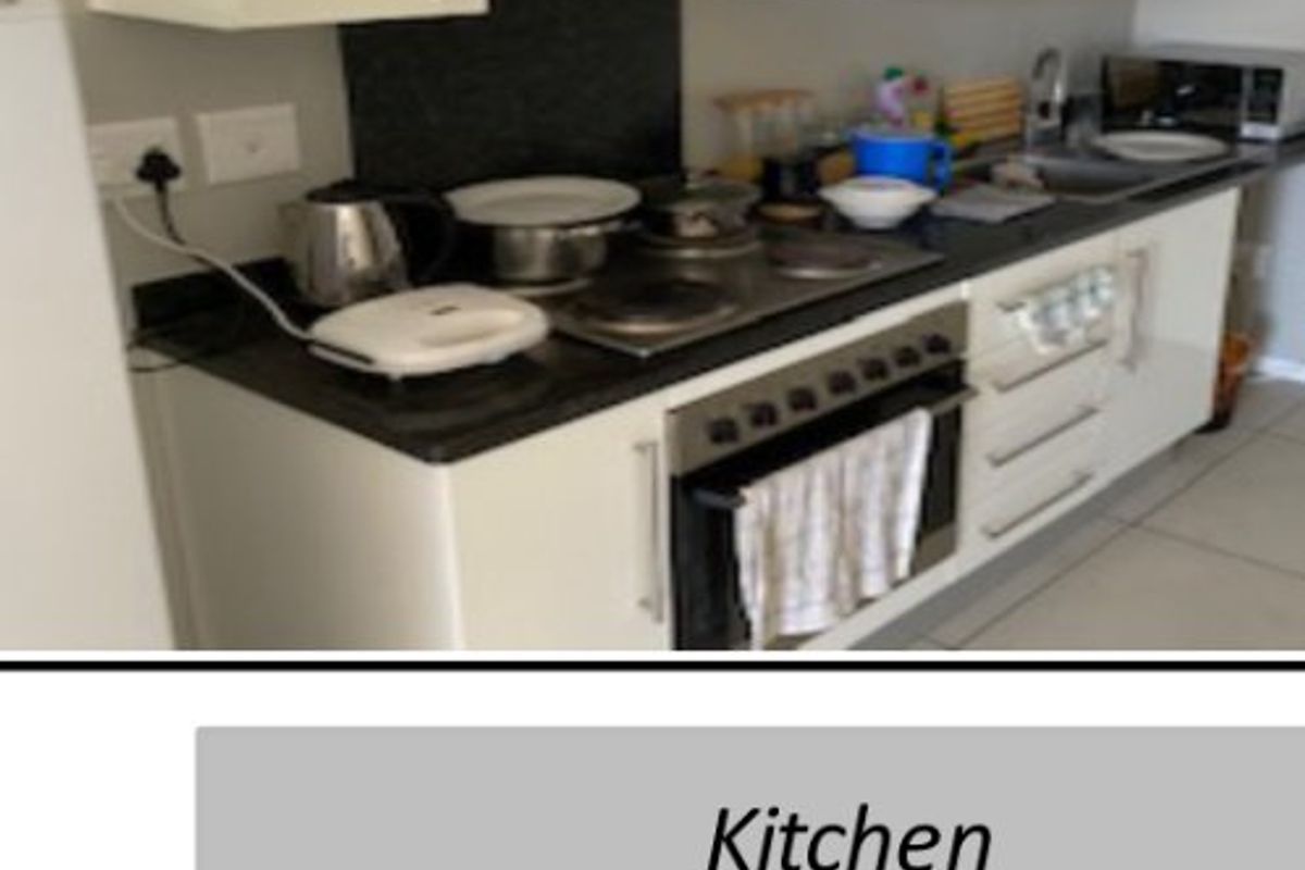 A compact kitchen featuring white cabinetry, dark stone countertops, an integrated electric hob, oven, and extractor fan.