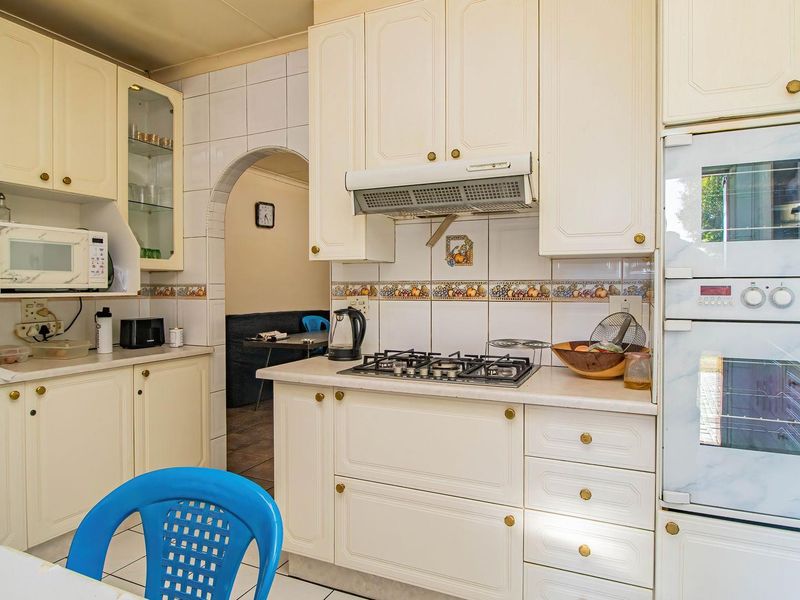 A functional kitchen featuring cream-colored cabinetry, a gas hob with extractor fan, built-in oven, and tiled backsplash, leading through an archway to adjacent living space.