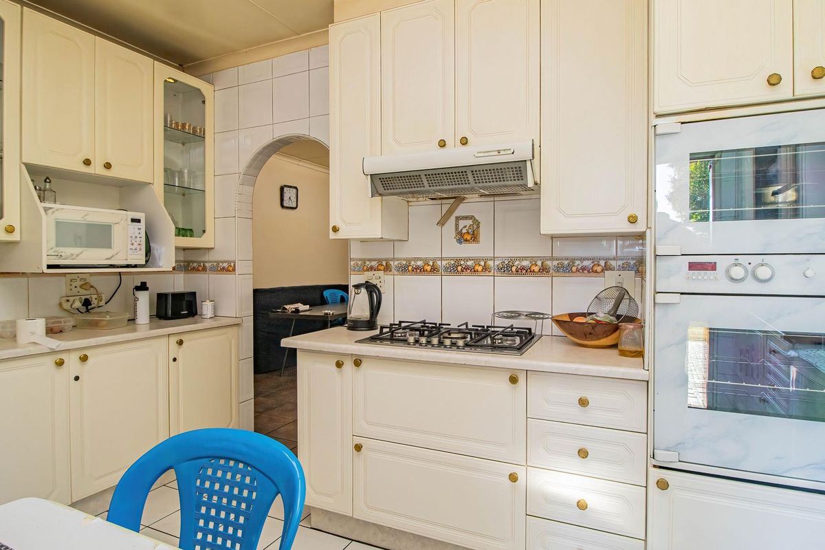 A functional kitchen featuring cream-colored cabinetry, a gas hob with extractor fan, built-in oven, and tiled backsplash, leading through an archway to adjacent living space.