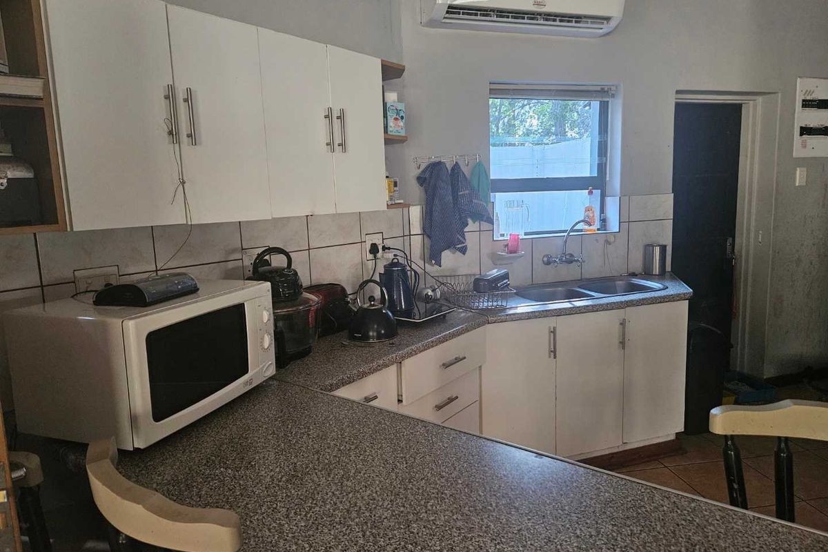 Functional kitchen featuring white cabinetry, granite-look laminate countertops, double basin sink, and a wall-mounted air conditioning unit.