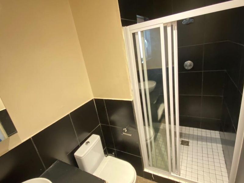 A compact bathroom featuring a shower enclosure with black wall tiles, a white toilet, and a wall-mounted mirror.