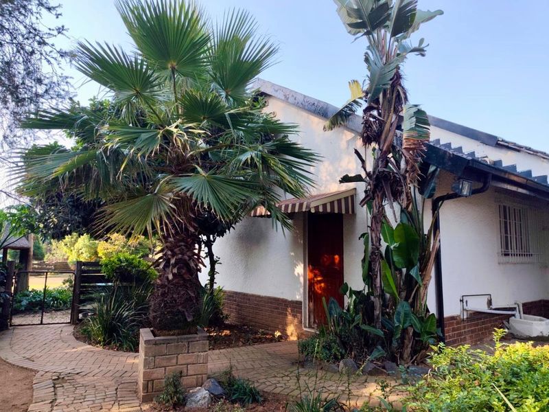 A rear exterior view of the cottage featuring brick paving, established garden landscaping, and a covered entrance area with a striped awning.