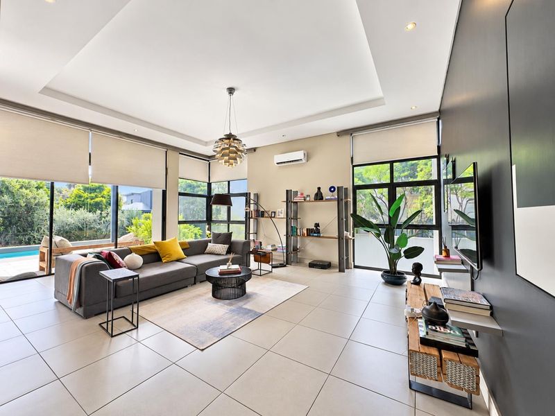 Spacious, modern living room featuring large windows, tiled floors, recessed ceiling detail, and split-system air conditioning with views of the outdoor pool area.