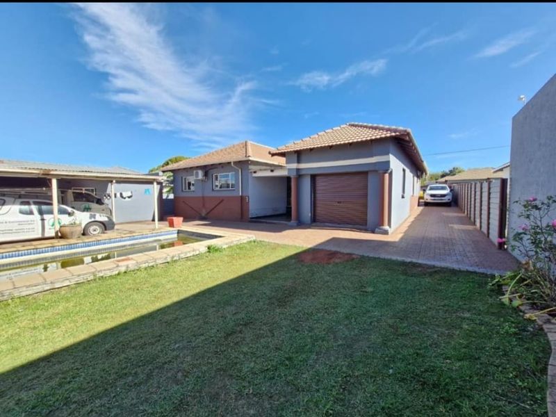 Rear exterior view featuring a swimming pool, paved driveway, attached garage, and carport area within a fenced property boundary.