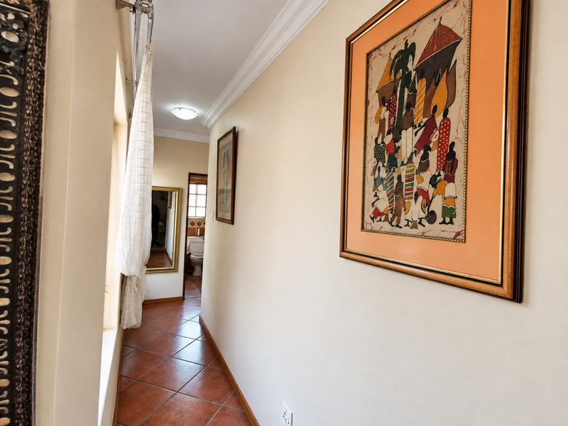 A well-maintained hallway featuring terracotta-style floor tiles, decorative ceiling cornicing, and access to an adjacent bathroom.