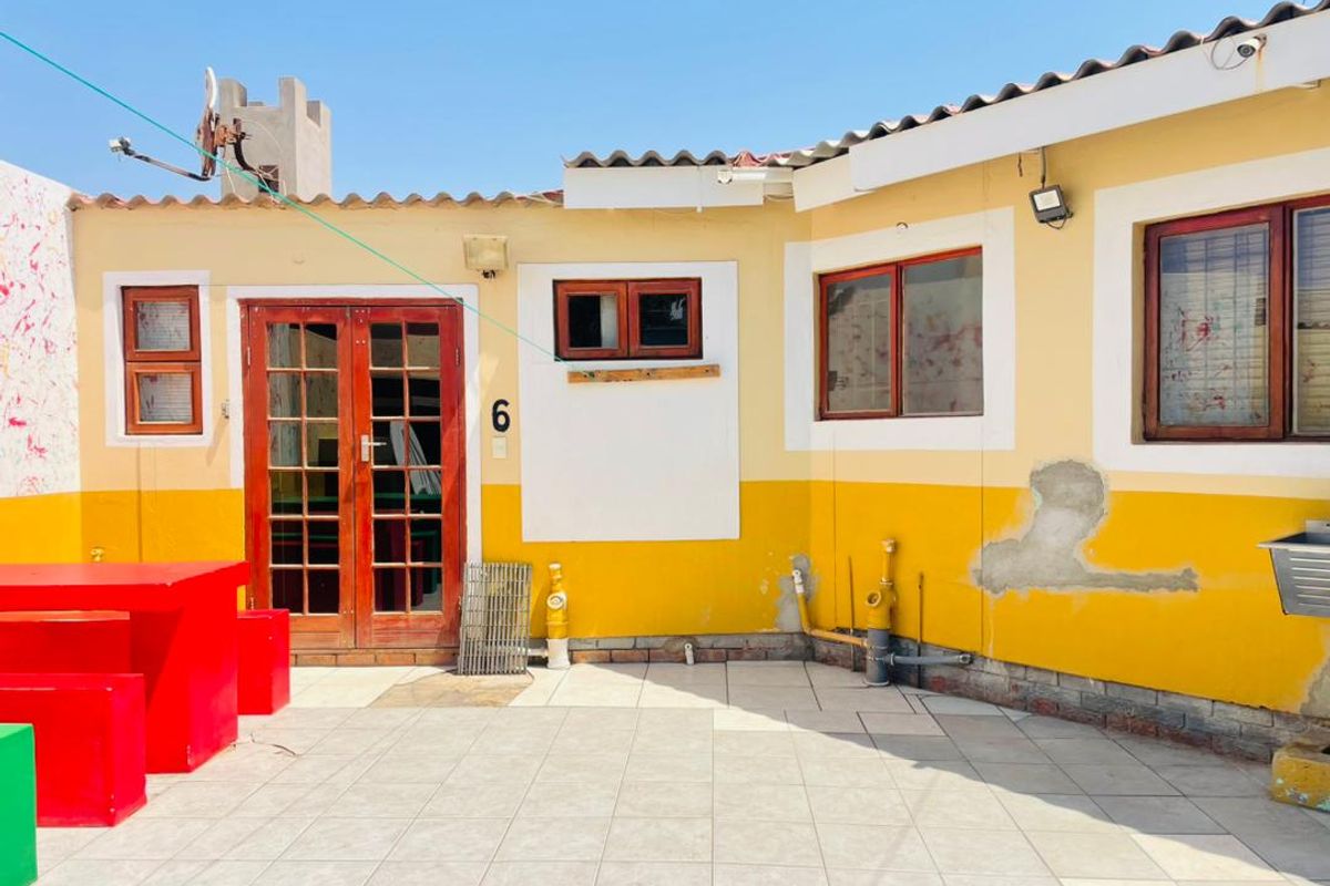 Rear exterior view of the property featuring a tiled patio area, timber-framed doors and windows, and visible exterior wall maintenance requirements.