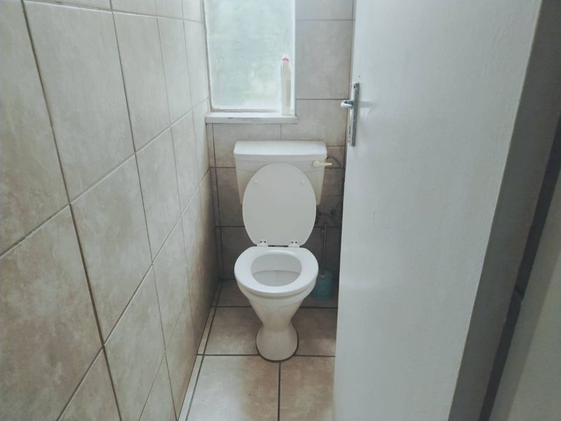 A compact, tiled bathroom featuring a standard toilet and an obscured glass window, requiring minor maintenance and cosmetic updates.
