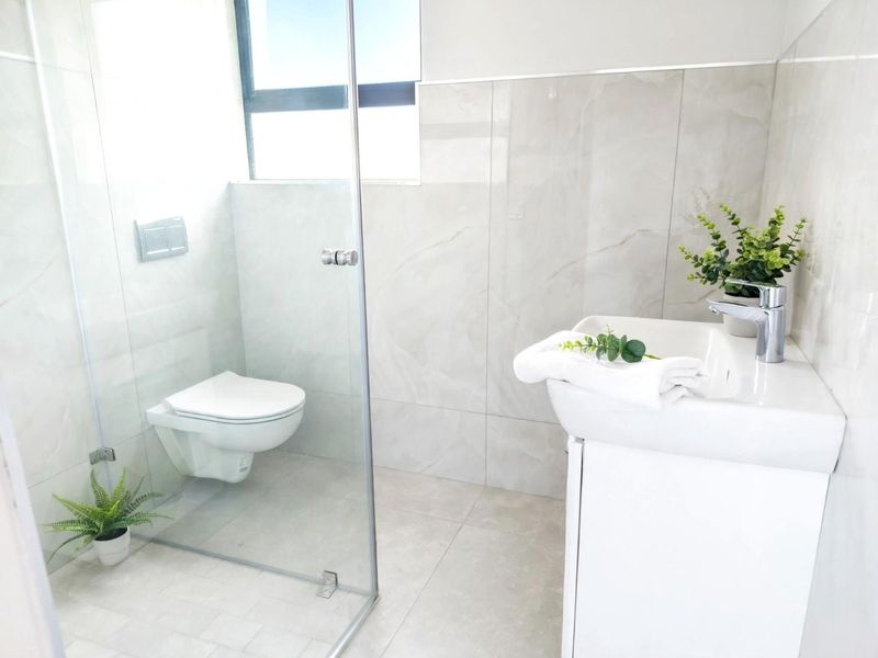 Modern bathroom featuring a wall-mounted toilet, glass shower enclosure, and a sleek vanity basin with contemporary porcelain tiling throughout.