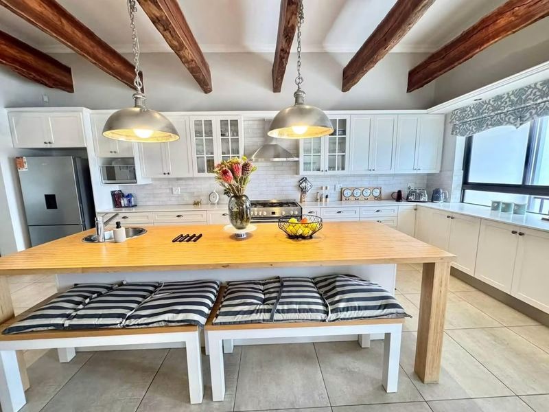 A well-appointed kitchen featuring white shaker cabinetry, subway tile backsplash, exposed timber ceiling beams, and a large central island with integrated seating.