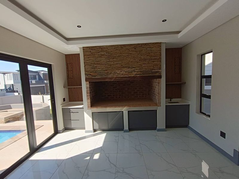 Modern indoor entertainment area featuring a built-in braai with stone cladding, slatted timber accents, sleek cabinetry, and large sliding doors opening to the pool area.