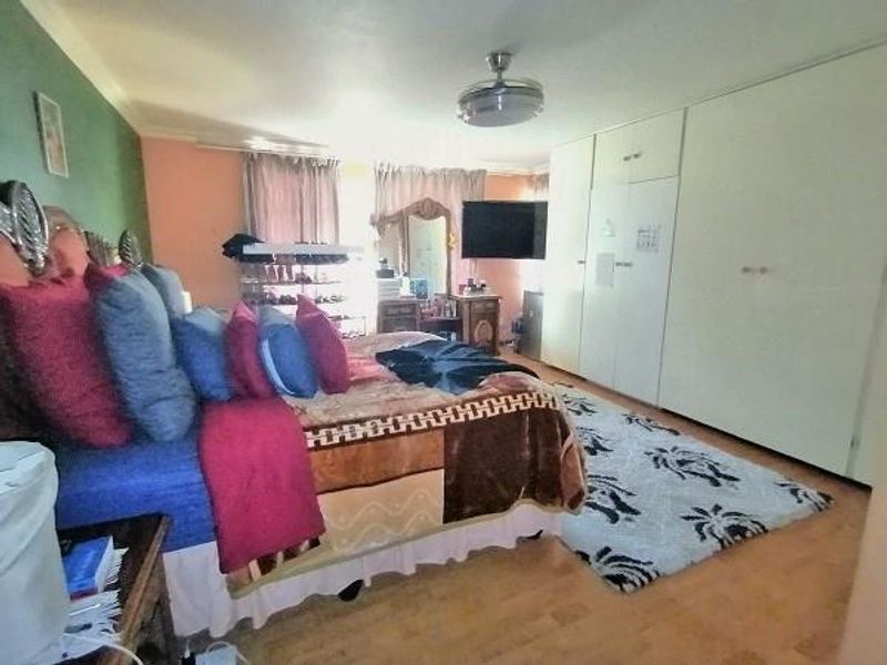 Spacious bedroom featuring extensive built-in cupboards, laminate flooring, and a ceiling fan, offering a functional layout with ample storage space.