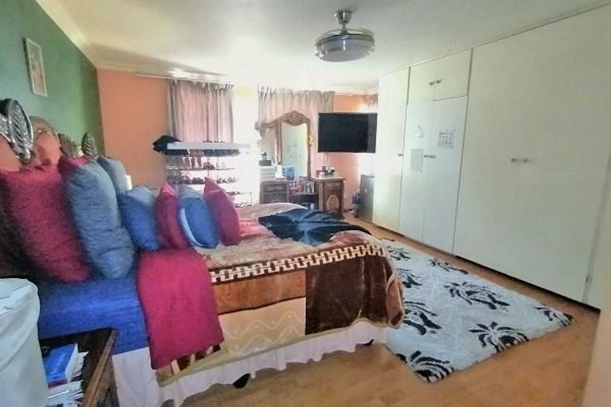 Spacious bedroom featuring extensive built-in cupboards, laminate flooring, and a ceiling fan, offering a functional layout with ample storage space.