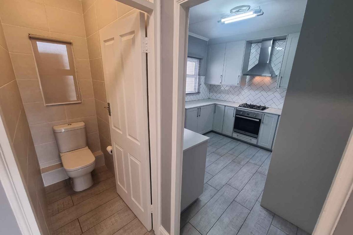 A modern kitchen featuring built-in cabinetry, gas hob, oven, and extractor fan, adjacent to a separate tiled toilet area.