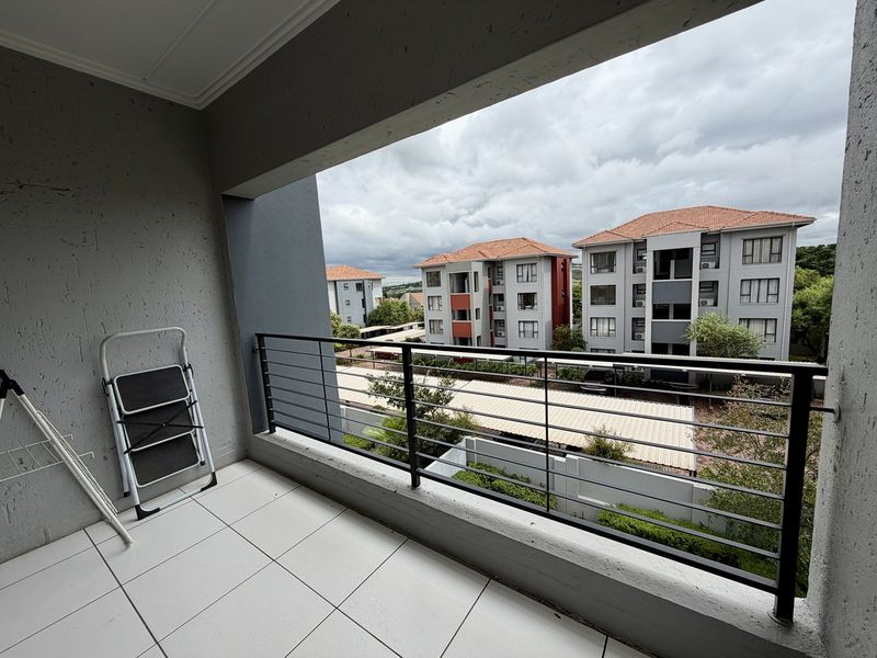 A covered balcony featuring tiled flooring and a metal balustrade, offering an elevated view of the surrounding apartment complex.