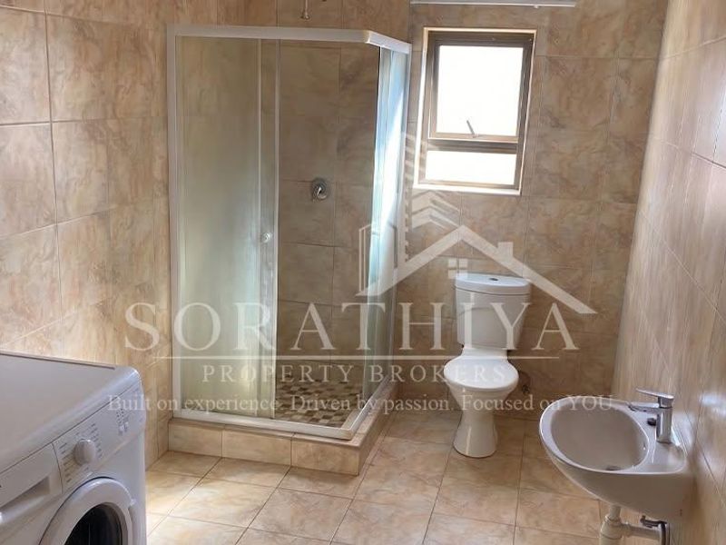A functional bathroom featuring a shower enclosure, toilet, and wall-mounted basin with full-height wall tiling.