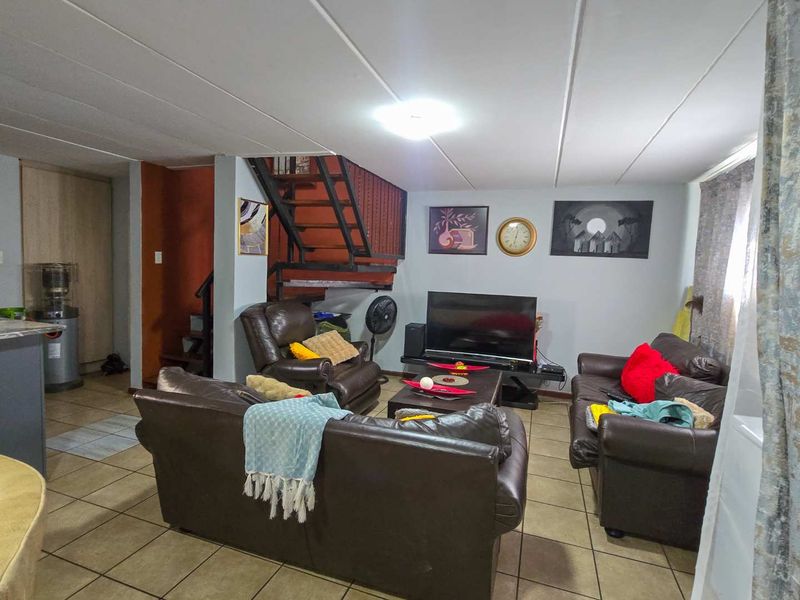 A living room area featuring tiled flooring and an internal metal staircase, providing a functional open-plan layout.