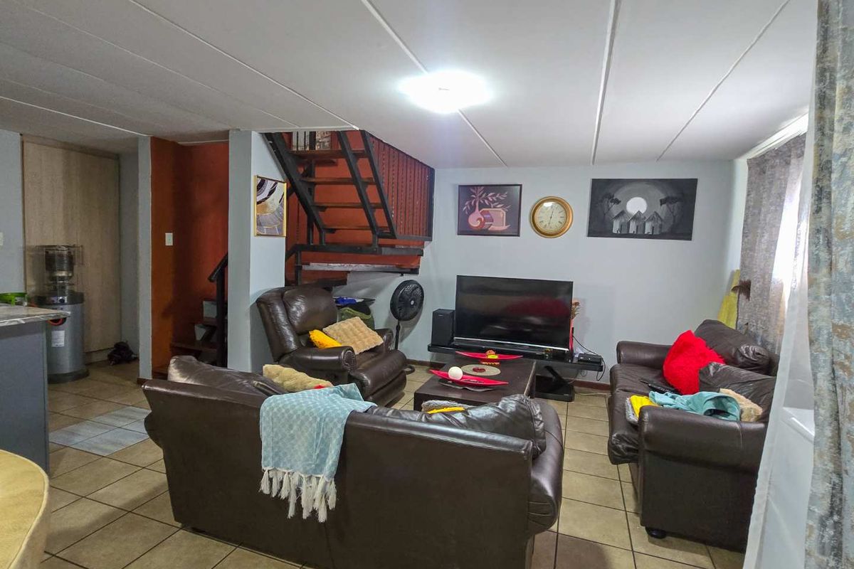 A living room area featuring tiled flooring and an internal metal staircase, providing a functional open-plan layout.