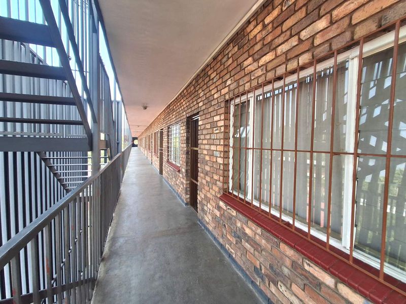 An exterior apartment building walkway featuring exposed brick walls, metal security bars on windows, and a metal staircase.