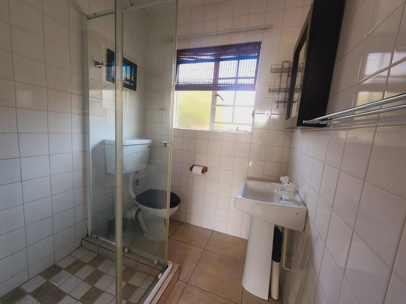A functional bathroom featuring a pedestal basin, a glass-enclosed shower, and tiled finishes throughout, offering a clean and practical layout.