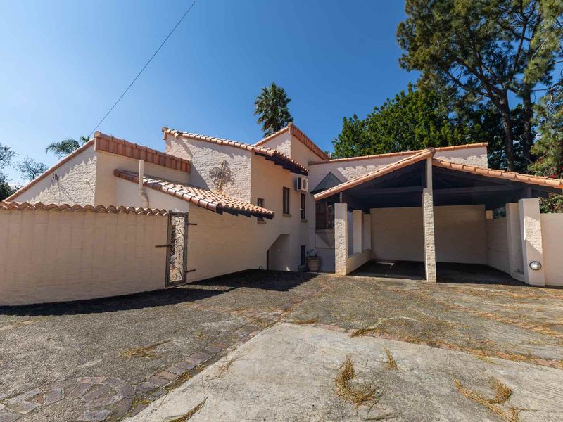 Front exterior view of the property featuring a covered carport, terracotta tiled roof, and a paved driveway with perimeter walling.