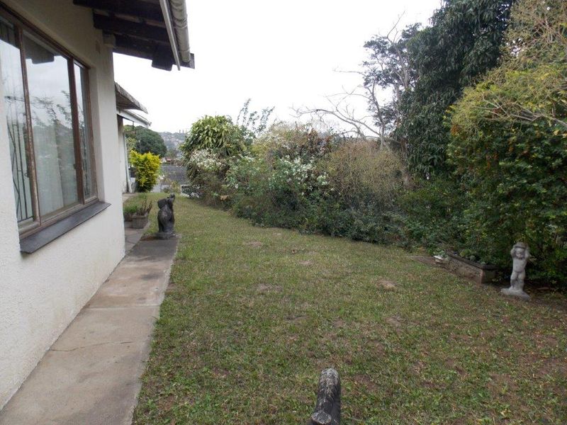 A view of the rear garden area featuring a concrete pathway alongside the house exterior and established garden landscaping.