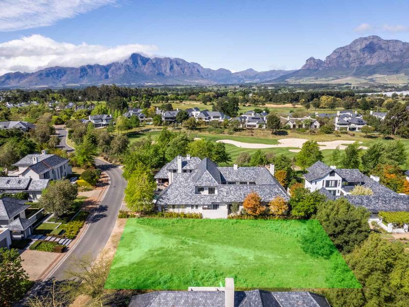 An aerial view of a vacant residential plot situated within a prestigious estate, featuring scenic mountain views and proximity to a golf course.