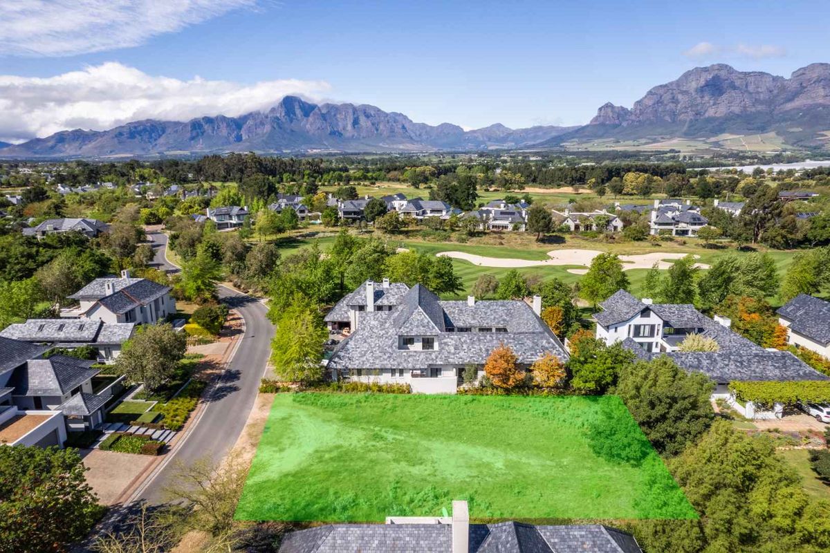 An aerial view of a vacant residential plot situated within a prestigious estate, featuring scenic mountain views and proximity to a golf course.