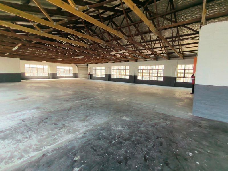 Spacious industrial open-plan warehouse area featuring exposed timber roof trusses, concrete flooring, and large steel-framed windows providing ample natural light.