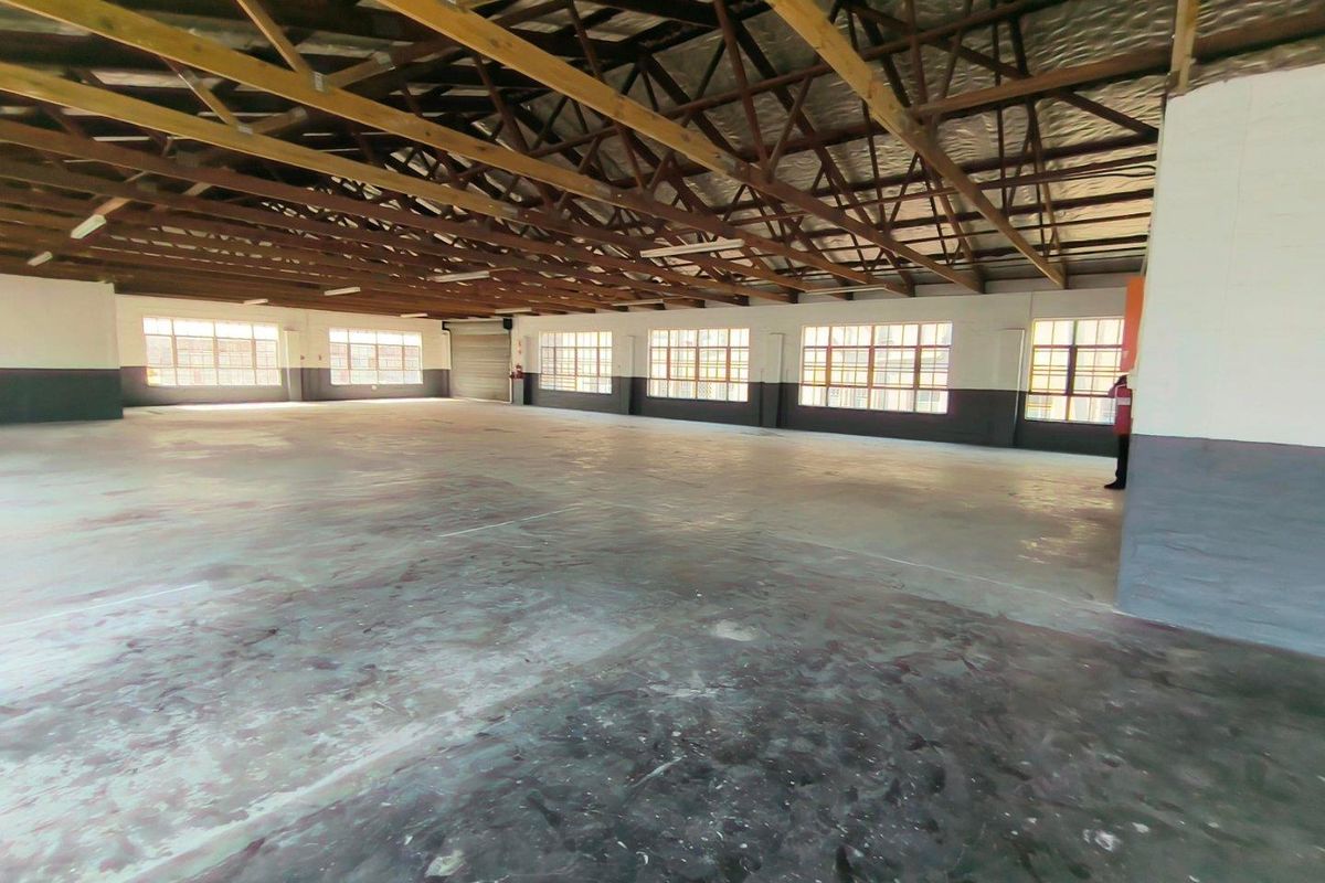Spacious industrial open-plan warehouse area featuring exposed timber roof trusses, concrete flooring, and large steel-framed windows providing ample natural light.
