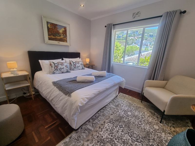 A well-maintained bedroom featuring classic parquet flooring, large window with natural light, and neutral wall finishes.