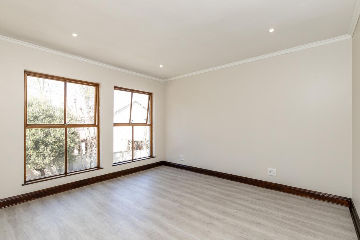 A bright, empty bedroom featuring light-toned laminate flooring, timber-framed windows, and recessed downlighting, providing a clean and neutral canvas for personalization.